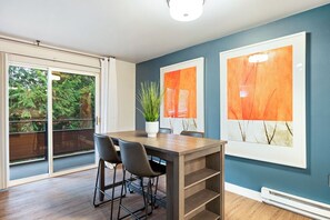 Uma sala de jantar moderna com uma mesa de madeira, cadeiras pretas e duas pinturas abstratas emolduradas na parede.
