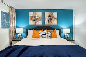 Quarto com cama, duas luminárias fixadas na parede e duas pinturas abstratas.
