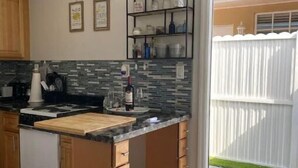 A kitchen with a central island, wooden cabinets, a tiled backsplash, and a sliding glass door leading to a backyard. - Modern Cozy Apartment in Hialeah Miami Int Airport (Hialeah)