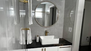 A modern bathroom with a white sink, gold handles, and a round mirror. - Spacious Apartment Central Located (Hialeah)