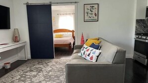 A modern living room with a sofa, a television, a bed, and a kitchen area. - Spacious Apartment Central Located (Hialeah)