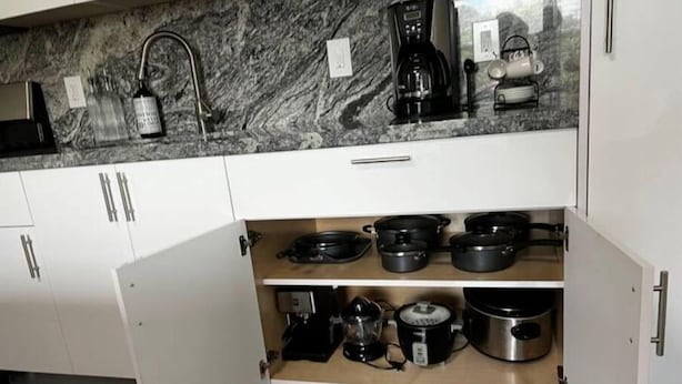 A kitchen with white cabinets, a marble countertop, and various cooking appliances including a coffee maker, kettle, and pots. - Spacious Apartment Central Located (Hialeah)