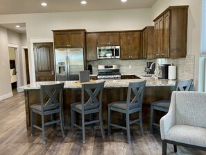 A modern kitchen with wooden cabinets, a stainless steel refrigerator, a microwave, a gas stove, and a bar area with bar stools.