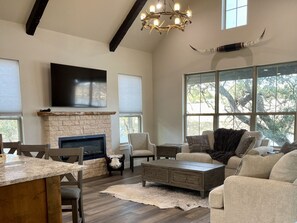 A spacious living room with a stone fireplace, comfortable seating, a large TV, and large windows offering natural light and views.
