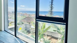 A view from a window with a clear sky, a tall tree, and a distant coastline. - Haus am Meer by Your Madeira Rentals (Paúl do Mar)