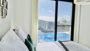 A bedroom with a large window, a bed with white and green pillows, and a view of a swimming pool. - Haus am Meer by Your Madeira Rentals (Paúl do Mar)