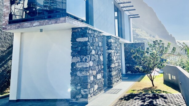A modern two-story house with a stone facade, large windows, and a balcony with a solar panel. - Haus am Meer by Your Madeira Rentals (Paúl do Mar)