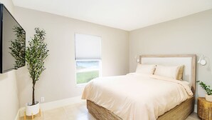 Un dormitorio con una cama, una planta en maceta, una ventana y una lámpara de pared.