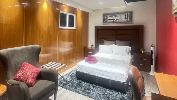 A modern bedroom with a bed, a chair, a desk, and a nightstand.