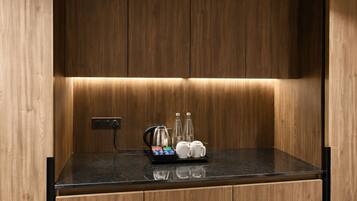 A kitchen with wooden cabinets, a black countertop, and a coffee station with a kettle, milk cartons, and mugs.