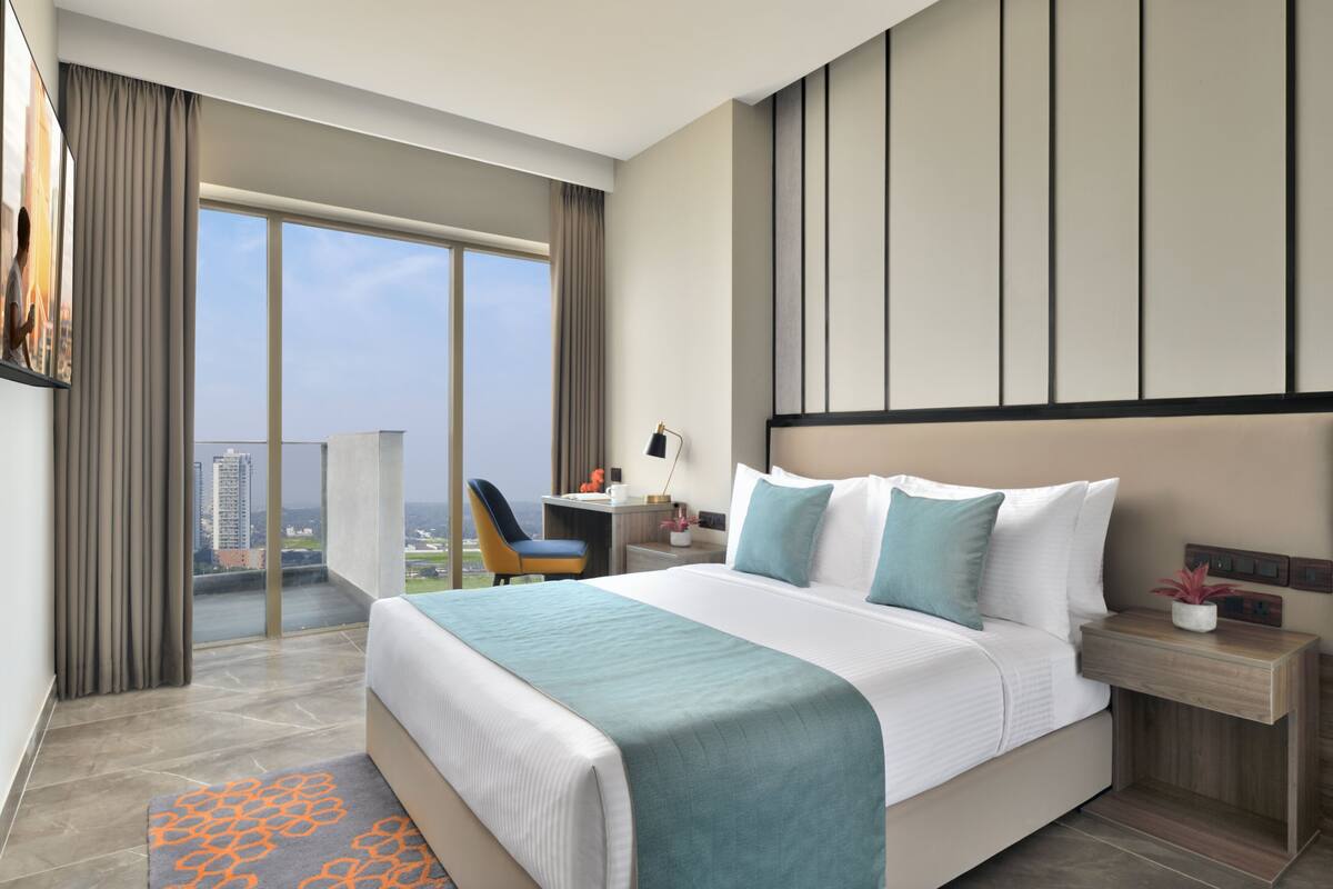 Ein modernes Hotelzimmer mit einem großen Bett, einem Schreibtisch, einem Sessel und Blick auf die Stadt.