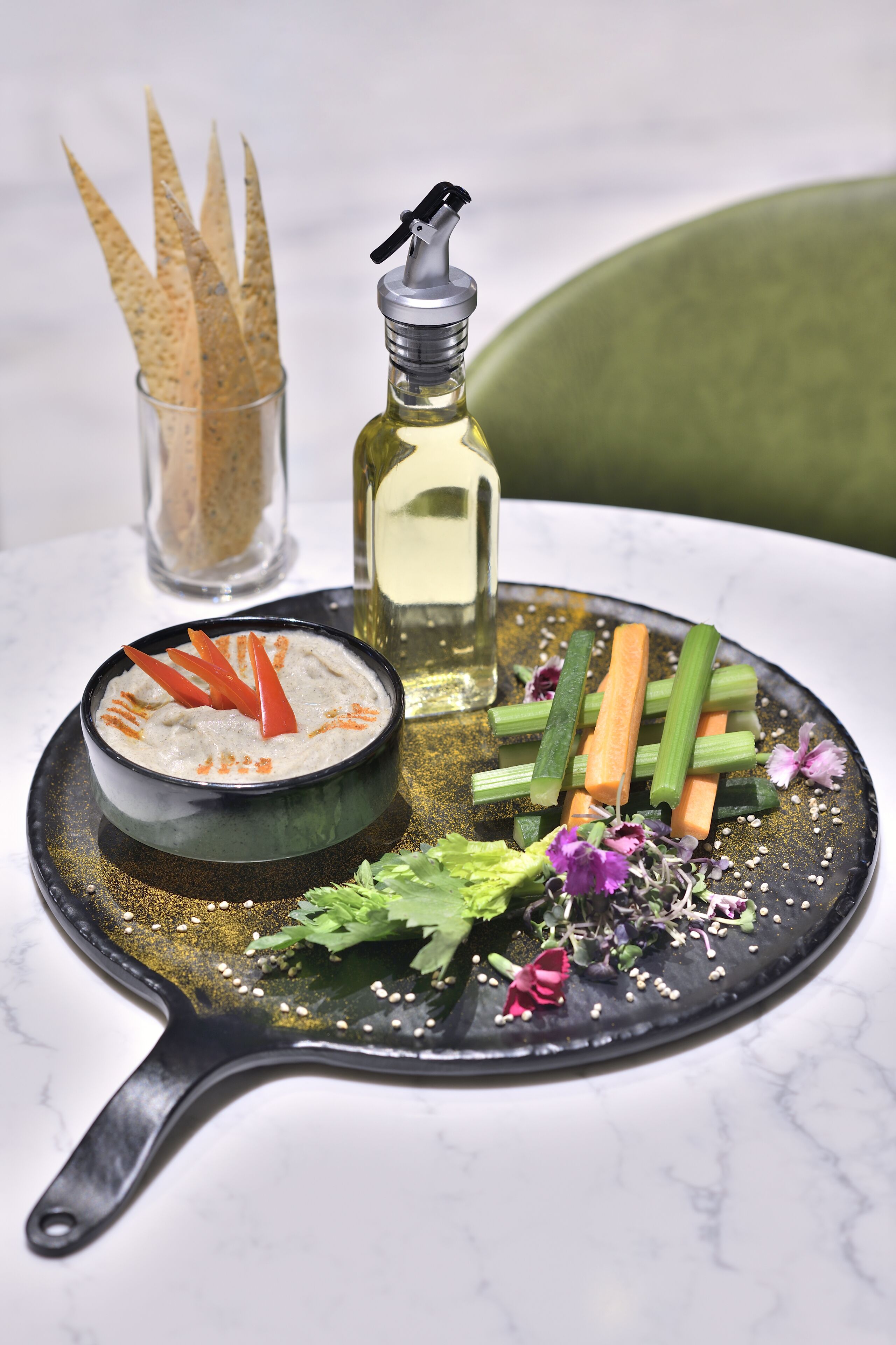 Une table à manger sur laquelle se trouve une poêle noire contenant un bol de sauce, décorée de légumes et d’herbes aromatiques.