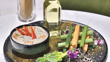Une table à manger sur laquelle se trouve une poêle noire contenant un bol de sauce, décorée de légumes et d’herbes aromatiques.