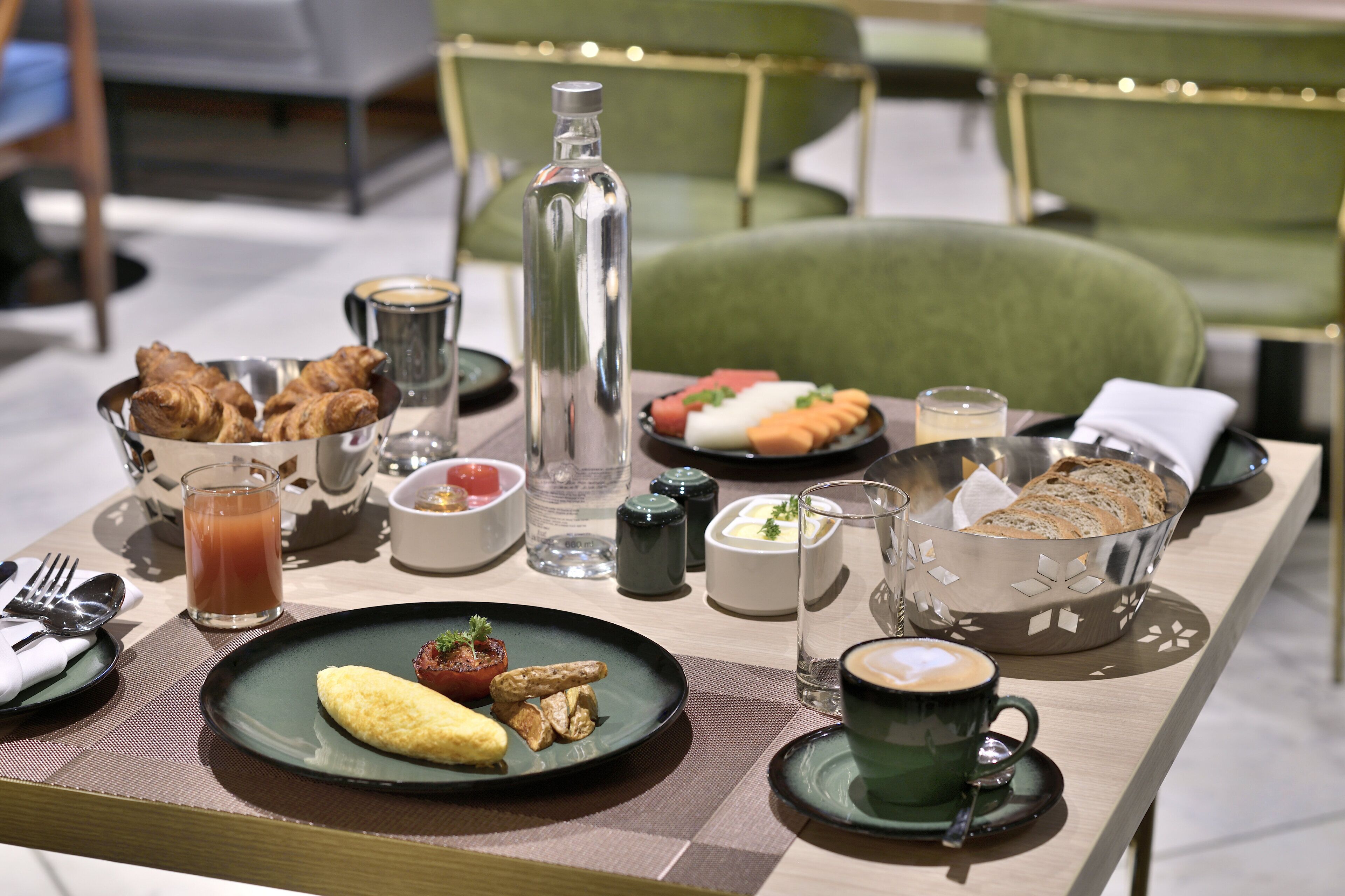 A breakfast table with croissants, a bottle, a bowl of fruit, and a coffee cup.