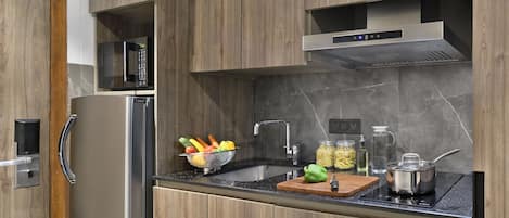 A modern kitchen with wooden cabinets, a stainless steel refrigerator, a microwave, a sink, and a stove.