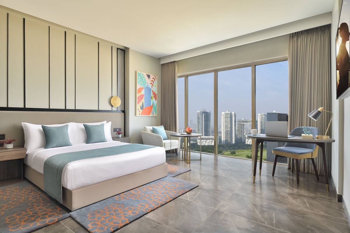 Ein modernes Hotelzimmer mit einem großen Bett, einem Schreibtisch, einem Sessel und Blick auf die Stadt.