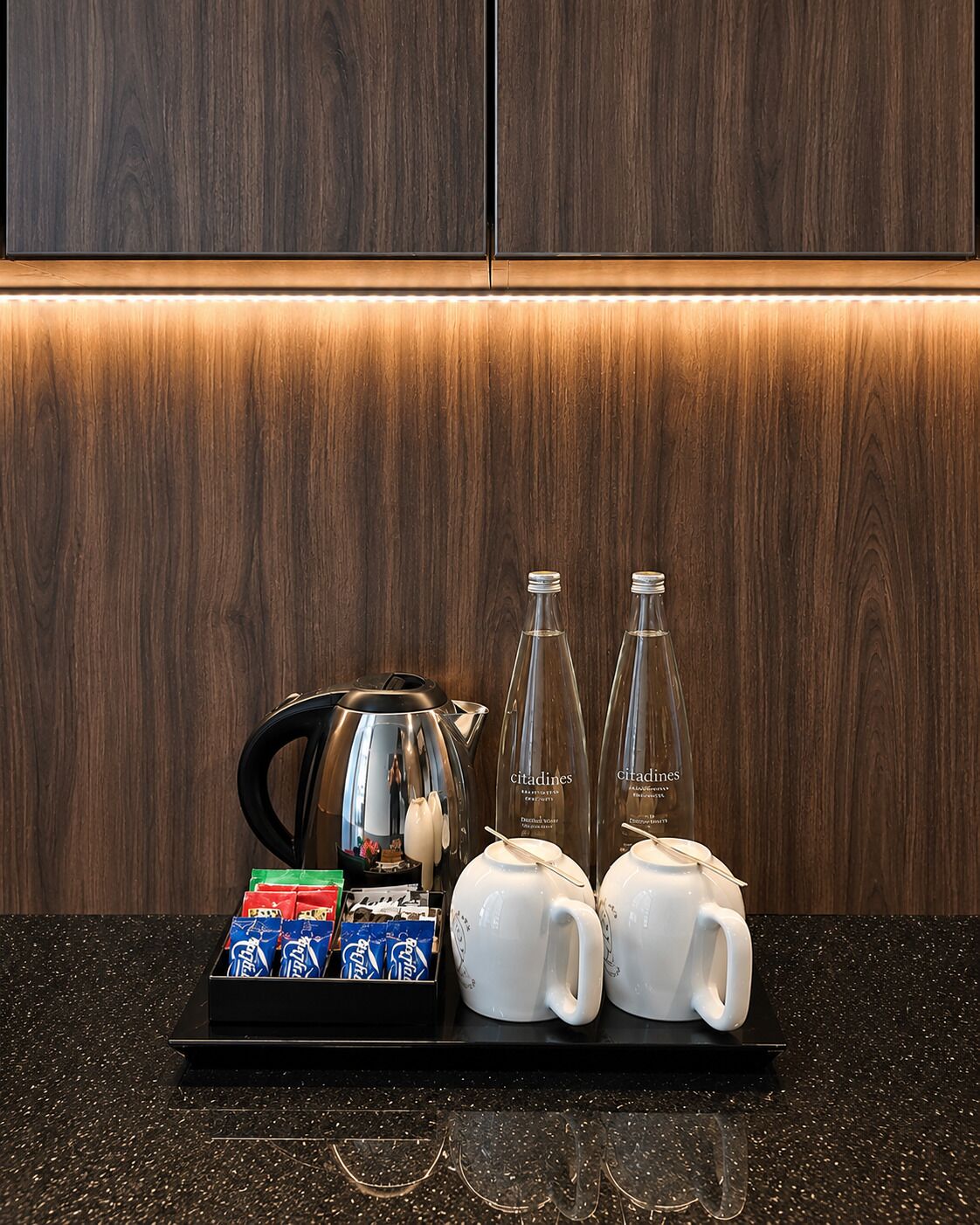 A coffee station with a kettle, two glasses, and a tray of coffee packets.