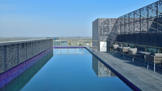 Une piscine sur le toit offrant une vue dégagée sur le paysage urbain, un mur orné de motifs et des espaces de détente en plein air.