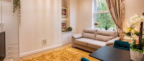 A living room with a sofa, a dining table, a TV, and a large window with curtains.