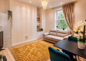 A living room with a sofa, a dining table, a TV, and a large window with curtains. - Botanic Apartment Central-Parking-sleep3 (Liverpool)