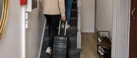 Um corredor com escada, um interruptor de luz na parede e um sapateiro.