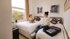A bedroom with two beds, a window with curtains, a radiator, and a suitcase on the floor. - Botanic Apartment Central-Parking-sleep3 (Liverpool)