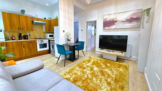 A modern living room with a grey sofa, a yellow shag rug, and a flat-screen TV. - Botanic Apartment Central-Parking-sleep3 (Liverpool)