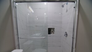A shower with a glass door, a handrail, and a showerhead. - The Capitol Inn - Destin Room - Queen bed (Tallahassee)