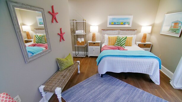 A bedroom with two beds, a bench, a mirror, starfish decorations, and a beach-themed painting. - The Capitol Inn - Destin Room - Queen bed (Tallahassee)