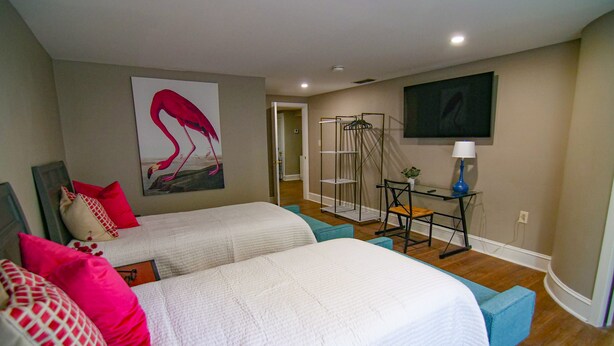 A bedroom with two beds, a desk with a chair, a TV, and a painting of flamingos. - The Capitol Inn - Orlando Room - 2 Twin beds (Tallahassee)