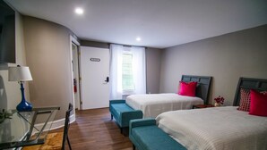A hotel room with two beds, a desk with a lamp, a bench, and a door labeled "ORLANDO". - The Capitol Inn - Orlando Room - 2 Twin beds (Tallahassee)
