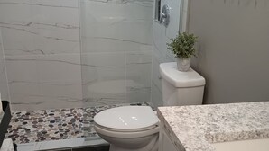 A modern bathroom with a shower, toilet, and marble-tiled floor.