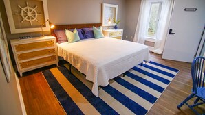 A bedroom with a bed, a nightstand, a dresser, a window with curtains, and a door labeled "Sarasota".