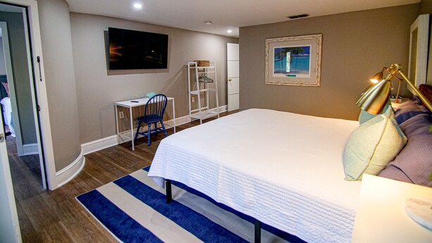 A bedroom with a bed, a desk, a chair, a shelf, and a painting on the wall.