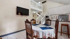 Un comedor con una mesa lista para cuatro personas, una escalera y una zona de cocina.