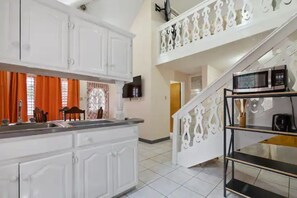 A kitchen with white cabinets, a black countertop, and a microwave on a shelf. - Shaw Park Gem Apt 12D (Ocho Rios,)