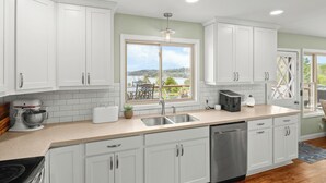 A modern kitchen with white cabinets, a large window offering a scenic view, a built-in dishwasher, and a countertop with a coffee maker.