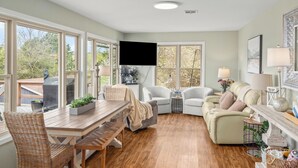A spacious living room with a wooden dining table, two sofas, and a TV mounted on the wall.