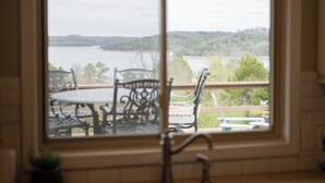A view through a window of a dining area with a table and chairs, overlooking a body of water and a forested landscape.