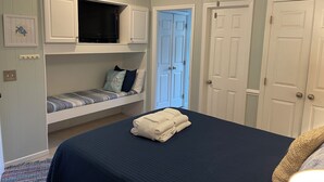 A bedroom with a bunk bed, a flat bed with a folded towel, and a blue door.