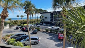 A parking lot with several cars, palm trees, and a building with a view of the ocean.