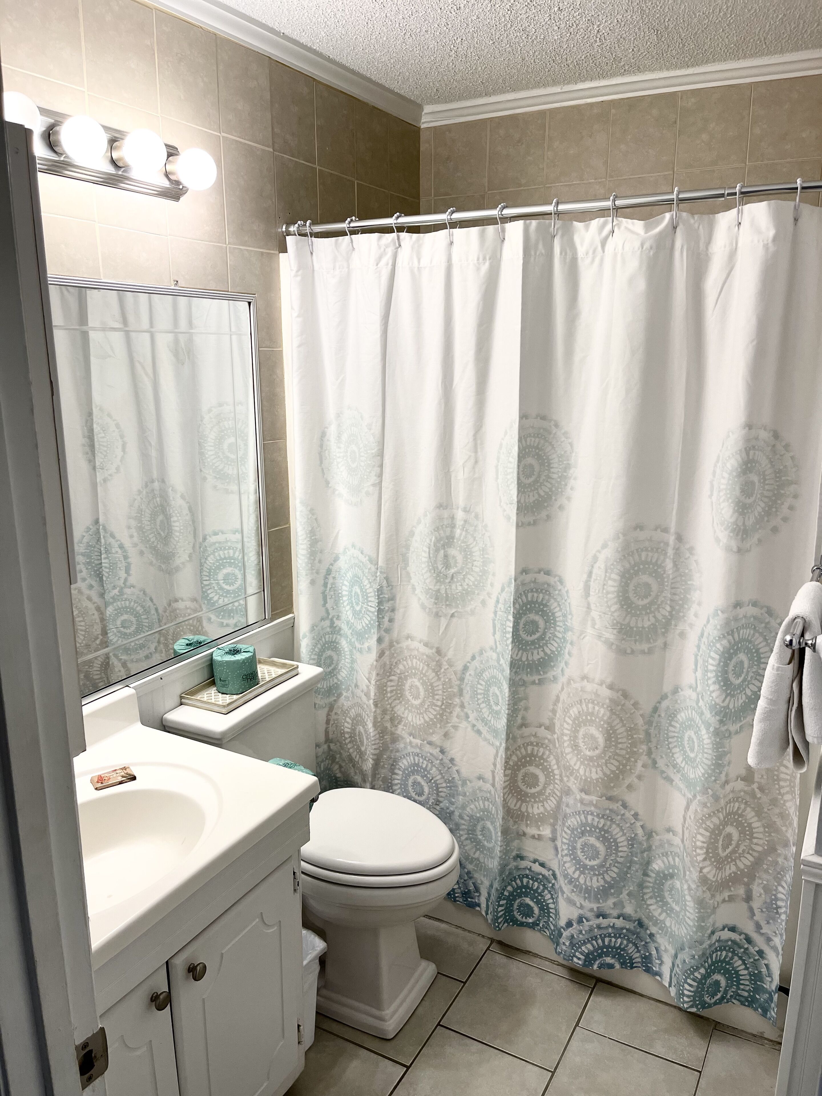 Un bagno con un lavandino bianco, un water, una tenda della doccia con motivo circolare e uno specchio con luci sopra.