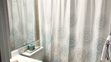 Un bagno con un lavandino bianco, un water, una tenda della doccia con motivo circolare e uno specchio con luci sopra.