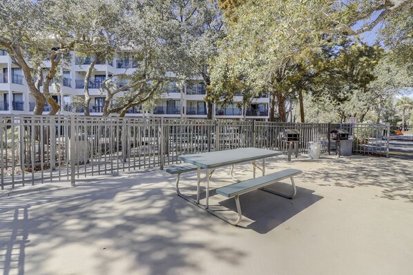 A park with a metal fence, a bench, and a trash bin.