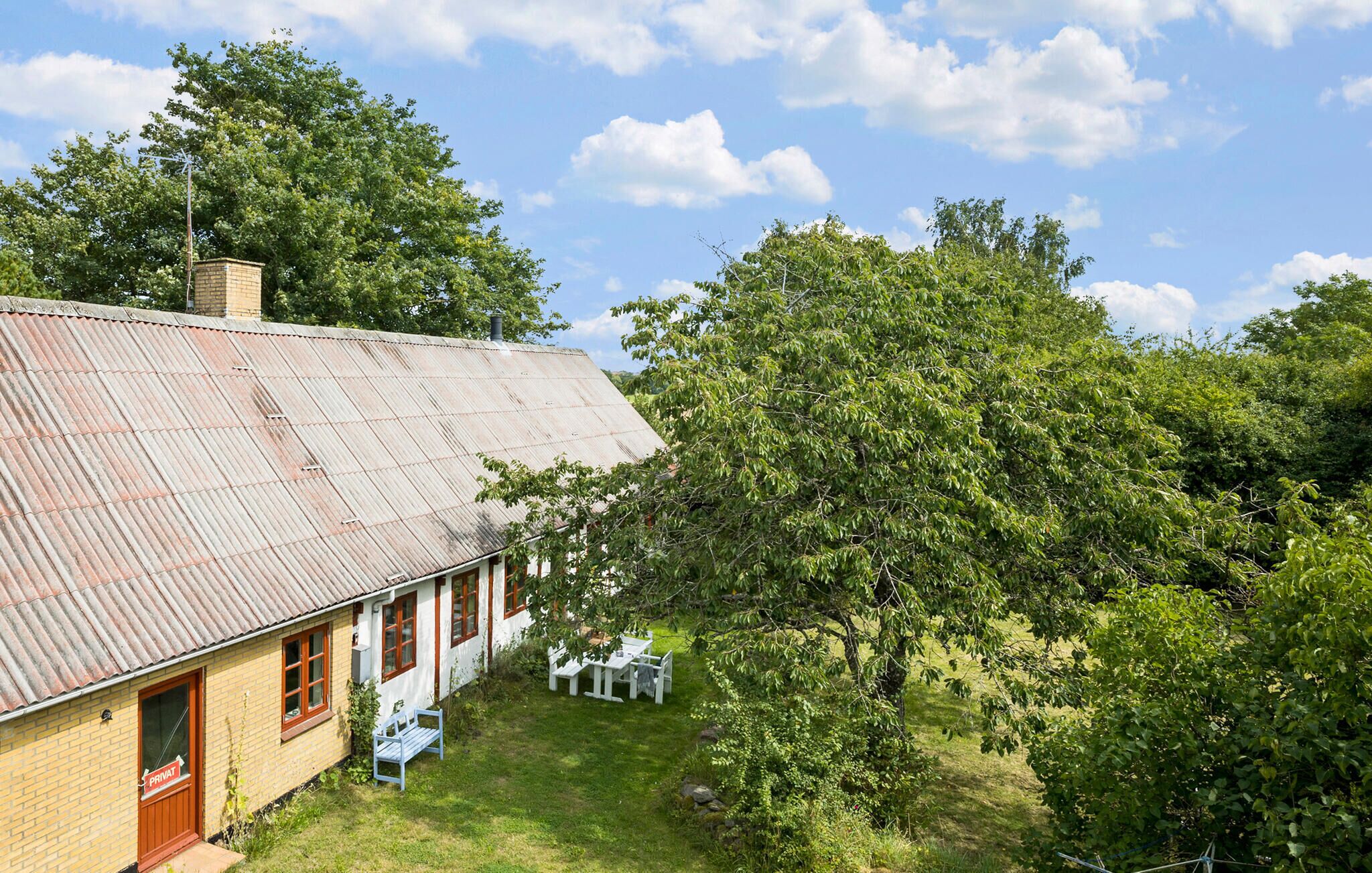 A rustic building with a corrugated metal roof, a brick chimney, and a small garden area with a bench and table.