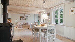 A cozy room with a wooden ceiling, a dining table with chairs, a sofa, and a large window with a view of trees.