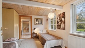 A bedroom with two beds, a wooden ceiling, a window with a view, and a framed picture on the wall.
