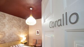 A hotel room with a bed, a nightstand with a lamp, two chairs, and a wall with the name 'Corallo'. - Epimonì B&b (Catania)