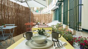 An outdoor patio with a yellow table set for two, surrounded by potted plants and a bamboo fence. - Epimonì B&b (Catania)