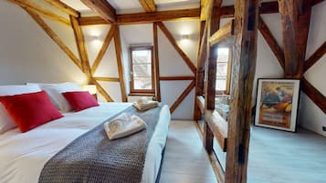 Une chambre avec un plafond en bois, un lit avec des oreillers blancs et rouges, une couverture tricotée et une affiche accrochée au mur.